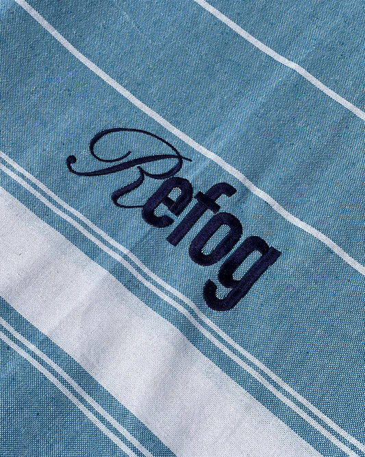 Detalle del logo bordado de Refog en toalla azul con rayas blancas