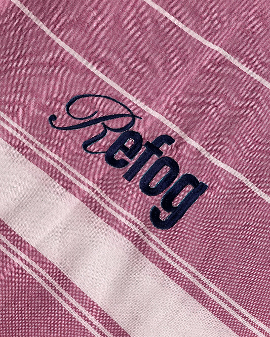 Detalle del logo bordado de Refog en toalla roja con rayas blancas