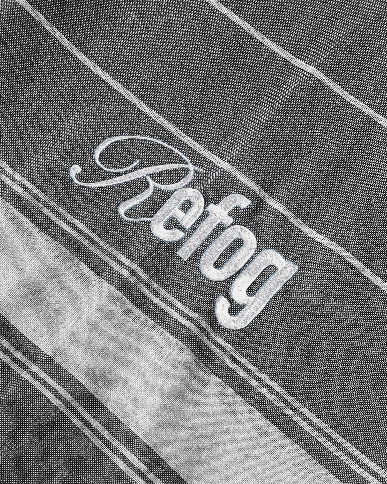 Detalle del logo bordado de Refog en toalla gris oscuro con rayas blancas