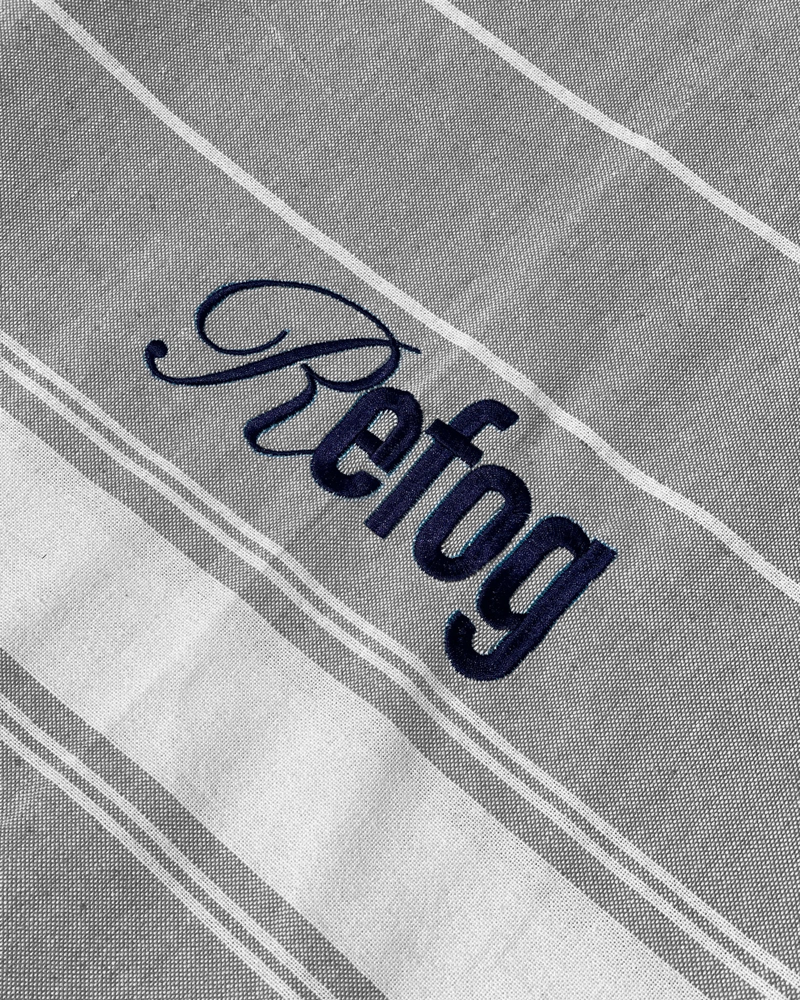 Detalle del logo bordado de Refog en toalla gris claro con rayas blancas