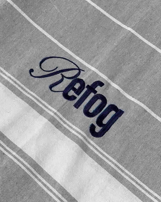 Detalle del logo bordado de Refog en toalla gris claro con rayas blancas