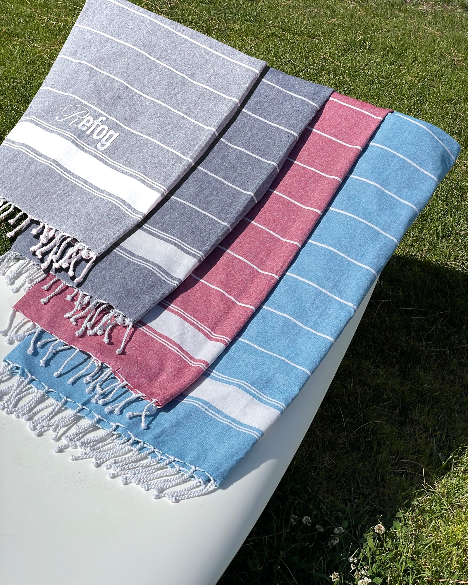 Toallas Refog en varios colores sobre exterior con diseño de rayas y flecos